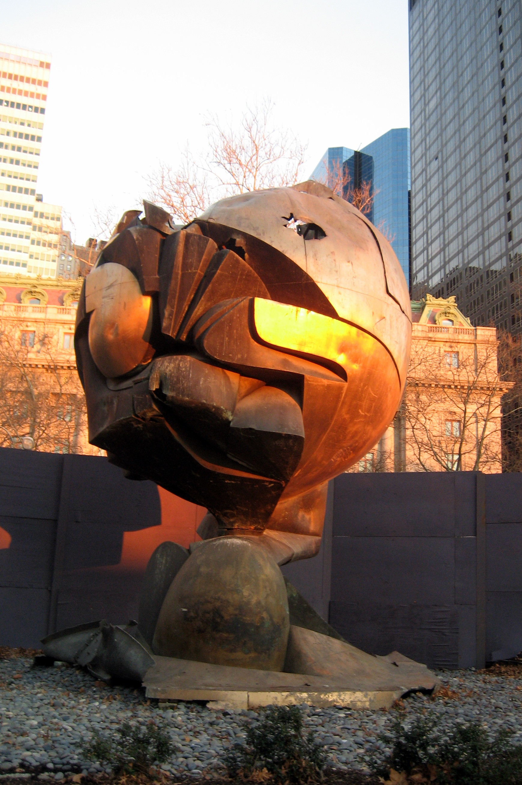 NYC - Battery Park: World Trade Center Sphere Perhaps the most emotionally charged piece in Battery Park is the temporary memorial to the events of 9/11. "The Sphere," a sculpture by Fritz Koenig that stood at the World Trade Center as a symbol of world peace, was relocated to Battery Park on March 11, 2002, some six months after the terrorist attacks. An eternal flame was added -- and lit -- on September 11, 2002, "in honor of all those who were lost," says an explanatory plaque. The Sphere, the plaque adds, "endures as an icon of hope and the indestructible spirit of this country." For more of my pictures of or about the World Trade Center, click here. For more details about 9/11, see this picture