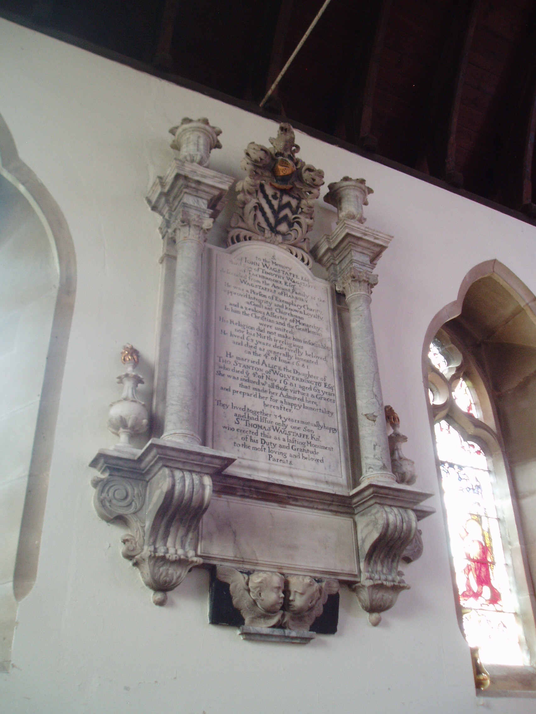 John Wagstaffe Memorial, Bishop's Tachbrook Monument on the south side of the sanctuary at Bishops Tachbrook commemorating John Wagstaffe (d.1681). St Chad's at Bishops Tachbrook dates largely from the Decorated and early Perpendicular periods, but is far older in origin with some traces of Norman work. It was restored in 1855 when the chancel was rebuilt. Inside the church has a fine set of Victorian windows by several different makers, including an early piece by Morris & Co and a fine east window by Heaton, Butler & Bayne commemorating Sir Charles Kingsley (author of 'The Water Babies') whose wife lived and died locally. There are also several wall monuments from the Baroque period, the most notable being that adorned with swags and putti commemorating Sir Thomas Wagstaffe. This fine church is normally kept locked outside of services.