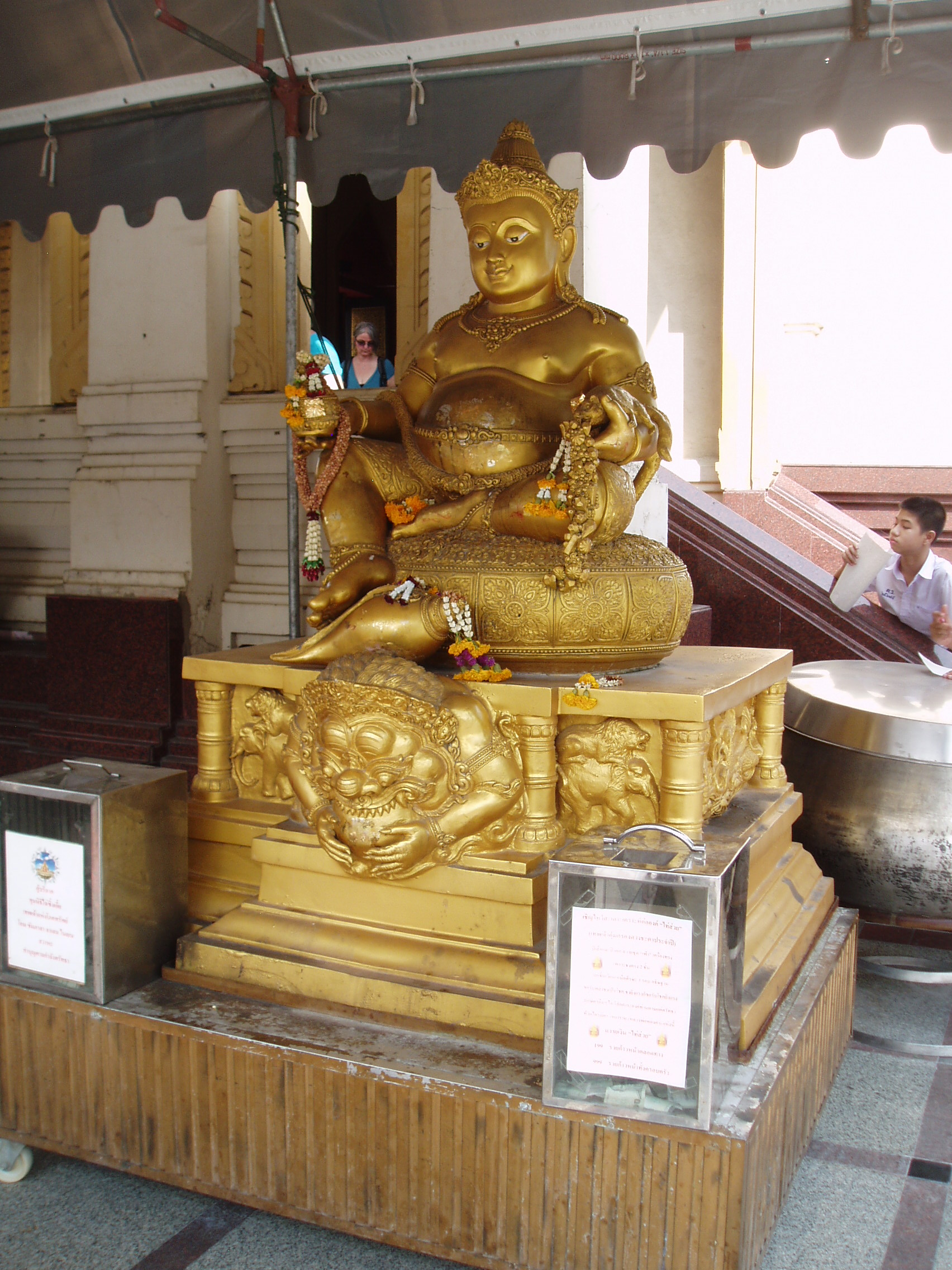 Buddha, Wat Triamit, Bangkok Wat Triamit was one of Bangkok's lesser temples until the amazing discovery of it's main attaction in 1955, when an old painted-stucco sculpture of the seated Buddha was being relocated to the temple; dropped by a crane during the process, the figure's stucco finished cracked, revealing beneath a beautiful solid gold statue, the largest in the World. The Golden Buddha is believed to date as far back as the 13th century, in the Sukhothai style. It is believed to have been moved to the previous capital Ayutthaya until it's sack by the Burmese, at which point the statue must have been disguised under a stucco layer to protect it from the invading forces who looted the city. It lay forgotten for a good two centuries in Bangkok before it's true importance was revealed again. Today it is housed in a brand new shrine at the Wat Triamit Temple complex in Bangkok's Chinatown. The new Temple takes the form of a terraced structure crowned by a golden-steepled tower, under which the Buddha has sat since his relocation here in February 2010. The new temple is quite stunning, especially since all it's gilt and marble was still less than a year old when we visited, a wonderful introdtuction to the glorious Buddhist sites of the city. en.wikipedia.org/wiki/Golden_Buddha_%28statue%29