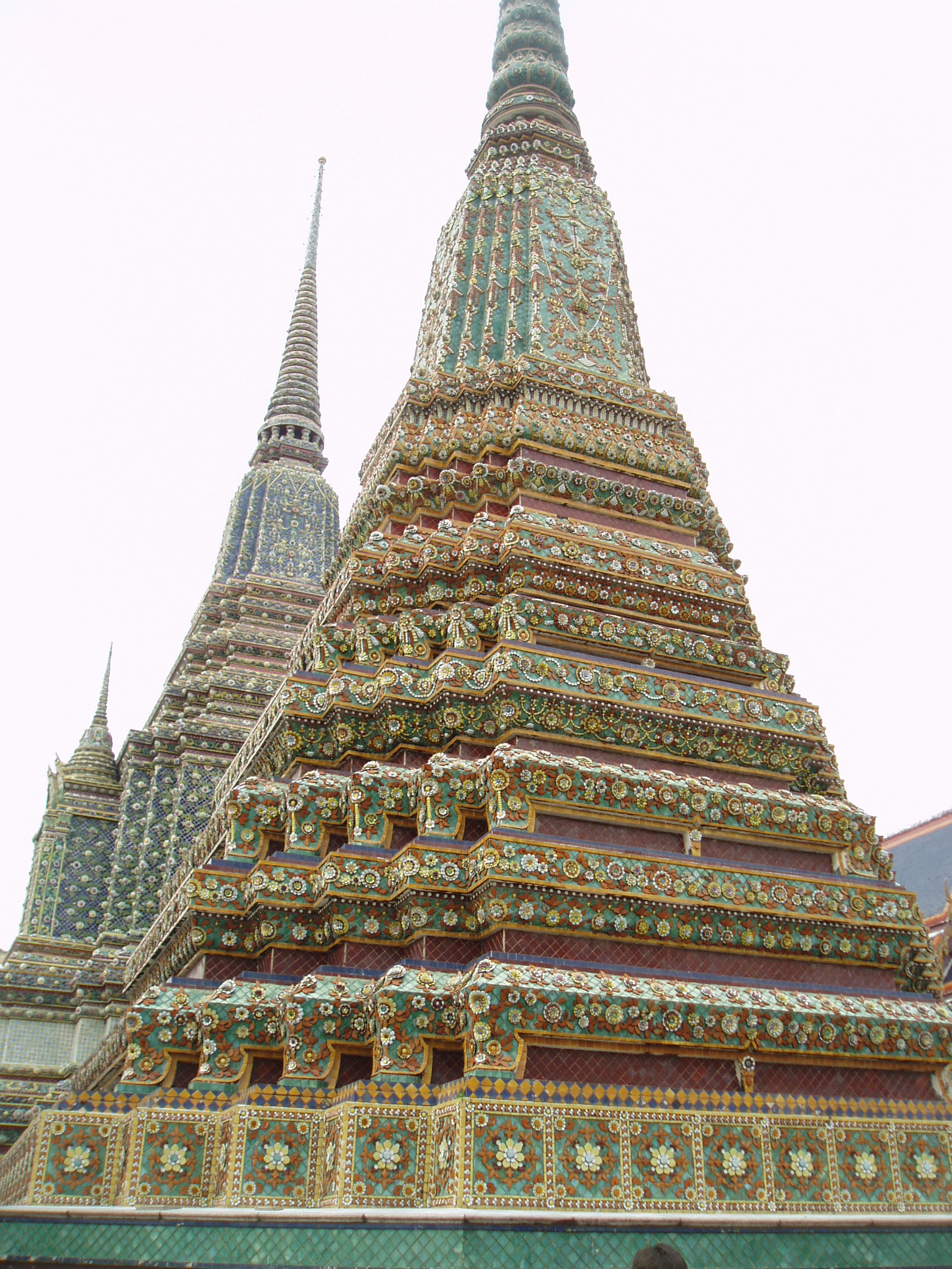 Ceramic Stupas, Wat Pho, Bangkok Wat Pho is the largest and oldest temple complex in Bangkok, and along with the temmple of the royal palace the most visited. The sprawling complex covers a huge area and it is quite easy to lose oneself within it's series of courtyards, gateways and stunning temple buildings. The present complex largely dates back to 1788, having been founded in response to the sacking of the former capital Ayutthaya by the Burmese in 1767 where a similar complex was destroyed. It is known as a place of learning and has a renowned school of Thai massage within the site. The temple complex is entered through one of many gateways guarded by huge Chinese statues, believed to have been imported as ballast on ships trading with China..The outer gates have fierce warrior figures, whilst the inner courtyards have the bizarre 'farang' ('foreigner') figures with their peculiar 'top hats', believed to represent the first European visitors to the east. Many of the inner courtyards are surrounded by a cloister containing over 400 sculptures of the seated Buddha, whilst the main Bot, the spiritual nucleus of the temple, is beautifully decorated within with frescoes of rich landscapes in red and gold. The biggest and most spectacular attraction of the temple however is the Hall of the Reclining Buddha, housing an enormous gilded recumbent figure of the Buddha over 160ft long, filling the entire centre of the chamber. en.wikipedia.org/wiki/Wat_Pho