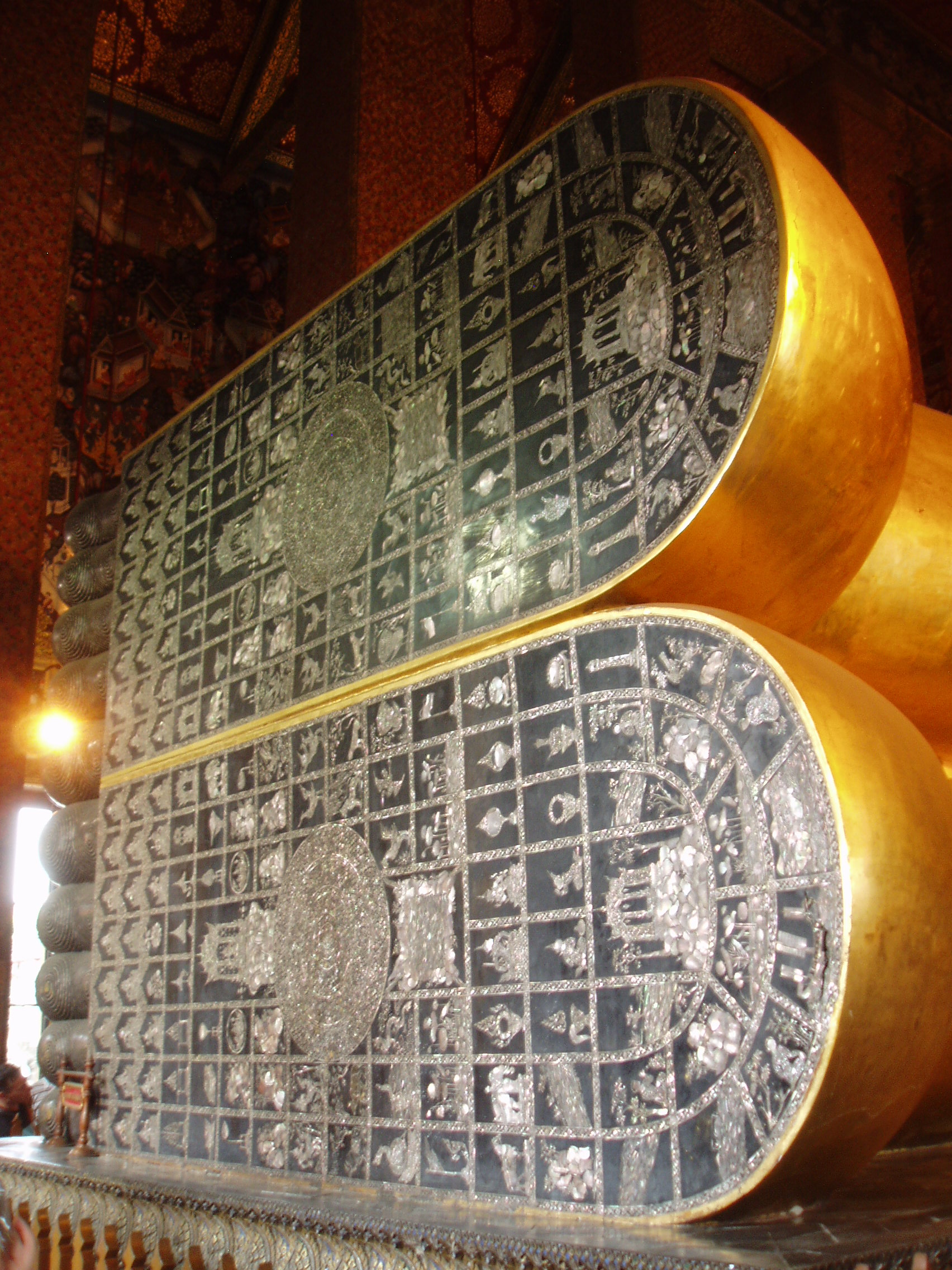 Feet of Reclining Buddha, Wat Pho, Bangkok Wat Pho is the largest and oldest temple complex in Bangkok, and along with the temmple of the royal palace the most visited. The sprawling complex covers a huge area and it is quite easy to lose oneself within it's series of courtyards, gateways and stunning temple buildings. The present complex largely dates back to 1788, having been founded in response to the sacking of the former capital Ayutthaya by the Burmese in 1767 where a similar complex was destroyed. It is known as a place of learning and has a renowned school of Thai massage within the site. The temple complex is entered through one of many gateways guarded by huge Chinese statues, believed to have been imported as ballast on ships trading with China..The outer gates have fierce warrior figures, whilst the inner courtyards have the bizarre 'farang' ('foreigner') figures with their peculiar 'top hats', believed to represent the first European visitors to the east. Many of the inner courtyards are surrounded by a cloister containing over 400 sculptures of the seated Buddha, whilst the main Bot, the spiritual nucleus of the temple, is beautifully decorated within with frescoes of rich landscapes in red and gold. The biggest and most spectacular attraction of the temple however is the Hall of the Reclining Buddha, housing an enormous gilded recumbent figure of the Buddha over 160ft long, filling the entire centre of the chamber. en.wikipedia.org/wiki/Wat_Pho