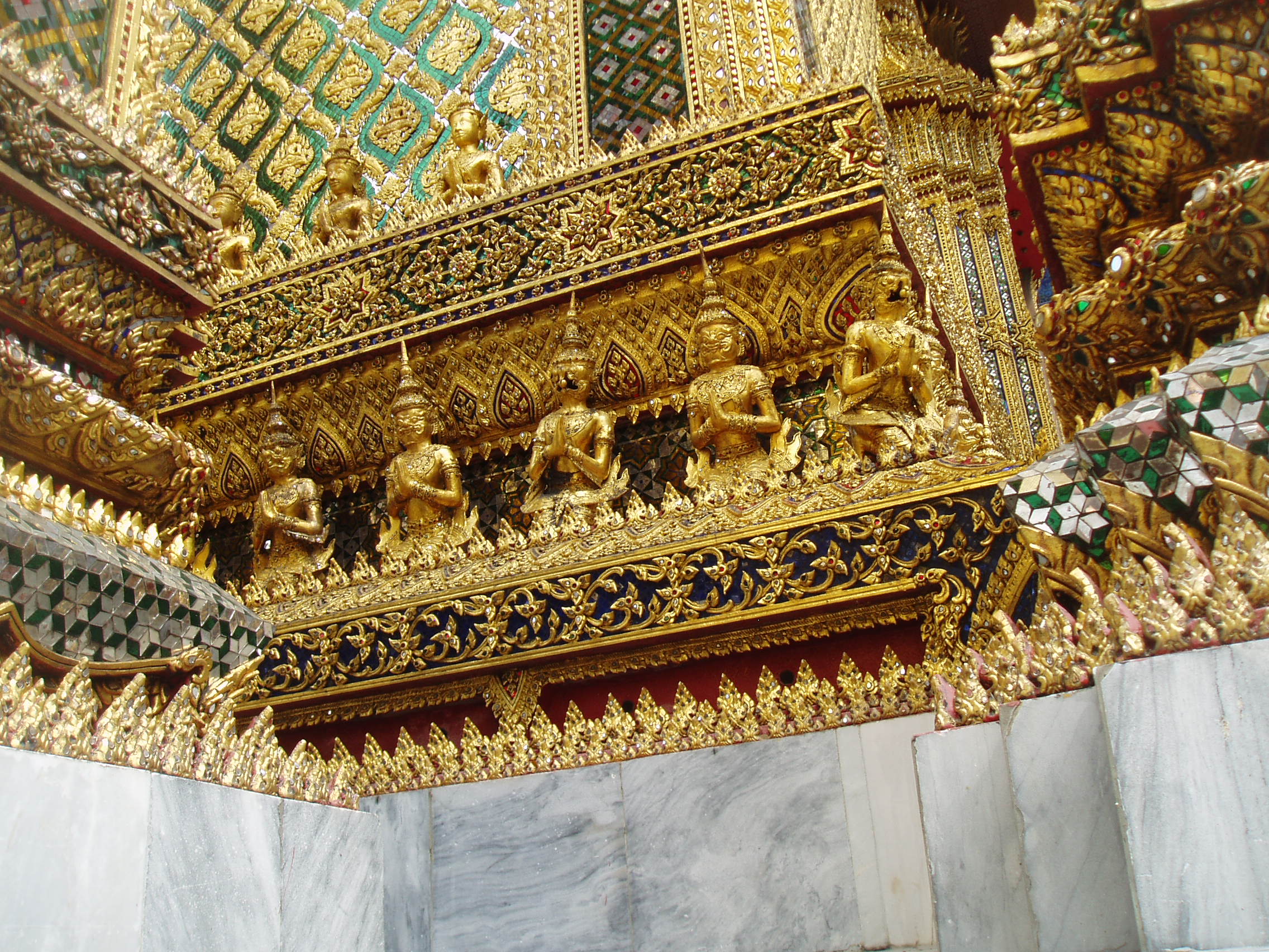 Gilded Decoration, Wat Phra Kaew, Bangkok Bangkok's most unmissable attraction is of course the Grand Palace, and most specifically the temple complex of Wat Phra Kaew (Temple of the Emerald Buddha), famed for it's riot of coloured and gilded ornament, paintings and sculptures; quite simply, so visually stunning there is nothing quite like it anywhere else! The Palace and Temple complex were begun in 1782, the year the capital was moved to Bangkok, and parts of the palace buildings betray 18th century European influence combined with traditional Thai style, such as the breathtaking gilt spires on the roof. Most of the interiors of the Palace itself are off limits to visitors since, although no longer the main residence of the thai monarchy, it is frequently used for state functions and ceremonies. The Wat Phra Kaew complex however is the greatest draw, famed for it's stunning architecture and the famous 'Yaksha' guardian figures that flank all the main entrances to the complex. These towering figures, with their rich colours and tapering crowns, represent demonic characters from the mythological epic the 'Ramakien', and are identifiable as distinct individuals, all here serving a benign, protective role. The Ramakien is also the subject for a stunning sequence of wall paintings within the cloister that encirlces the entire site, illustrating in minute detail the battles of the heroic monkey warriors, led by the monkey god Hanuman, against the demonic armies and kingdoms of Tosakan. The Temple of the Emerald Buddha itself forms the largest structure and contains the venerated (though small) Buddha image. The complex contains several other iconic buildings clad in sumptuous decor, most notably the library or 'mondop' with it's gilt spire along with the great golden stupa. The temple complex is technically a royal chapel rather than a working monastery like most Thai temples as it has no resident monks (the sheer volume of visitors leaves little room for anyone else anyway!). en.wikipedia.org/wiki/Wat_Phra_Kaew en.wikipedia.org/wiki/Grand_Palace