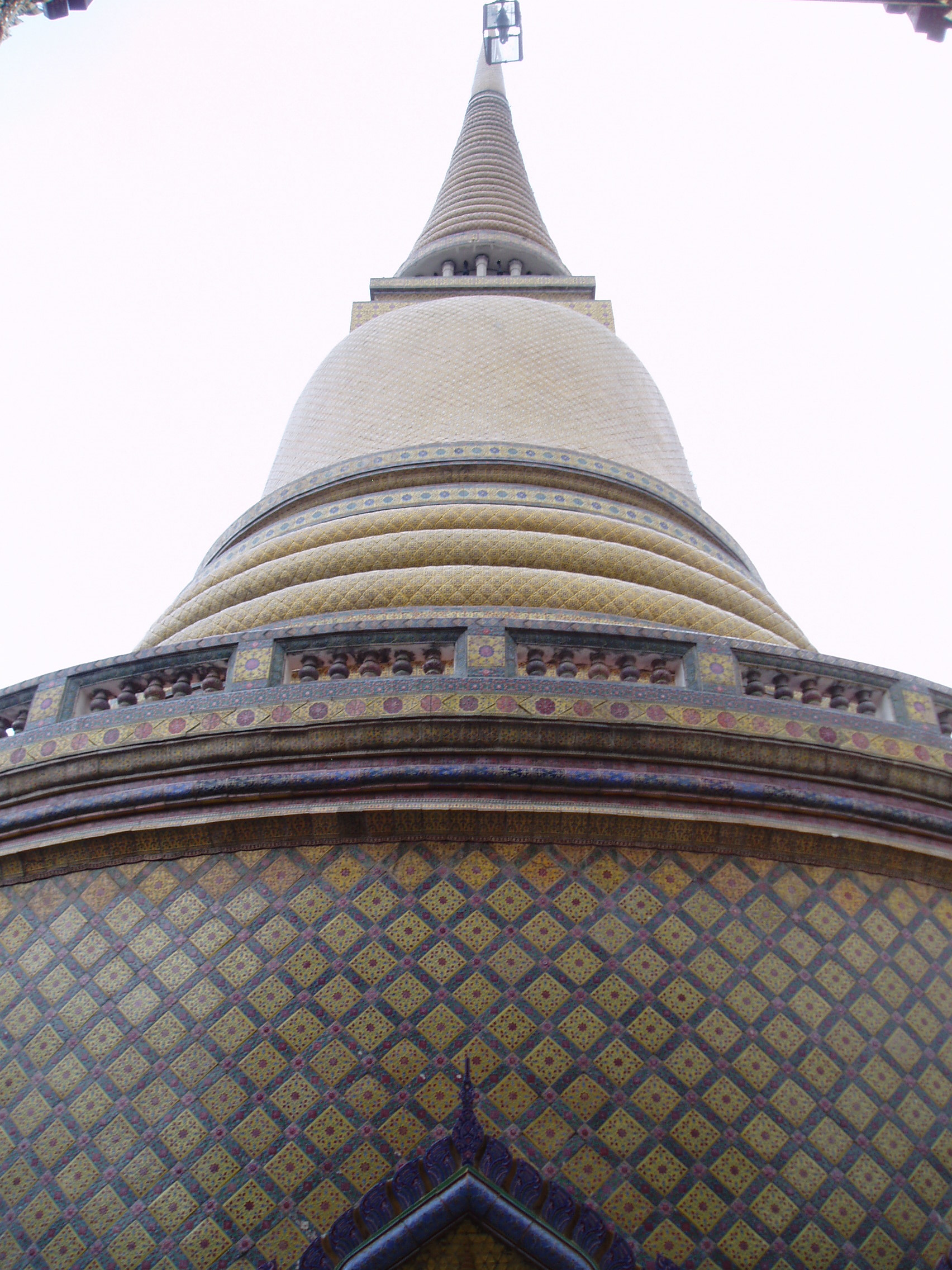 Main Stupa, Wat Ratchabophit, Bangkok Wat Ratchabophit is one of the most unusual temples in Bangkok; built in the latter half of the 19th century it shows marked European influence in certain areas, such as the neo-gothic interior of the main bot (prayer hall) and many of the monuments in the adjoining Royal Cemetery, that includes a domed classical style tower and pinnacled gothic steeples amongst more traditional Thai and Khmer style structures. The centrepiece of the Temple is the huge tile-covered stupa that grows from the heart of the complex and is surrounded by a tight circular courtyard. The surrounding structures are richly decorated and gilded with typical Thai richness. The entrance gates to the temple compound have carved and painted door panels with bizarre figures that appear to be 'farang' (foreign/European) guards holding rifles! en.wikipedia.org/wiki/Wat_Ratchabophit