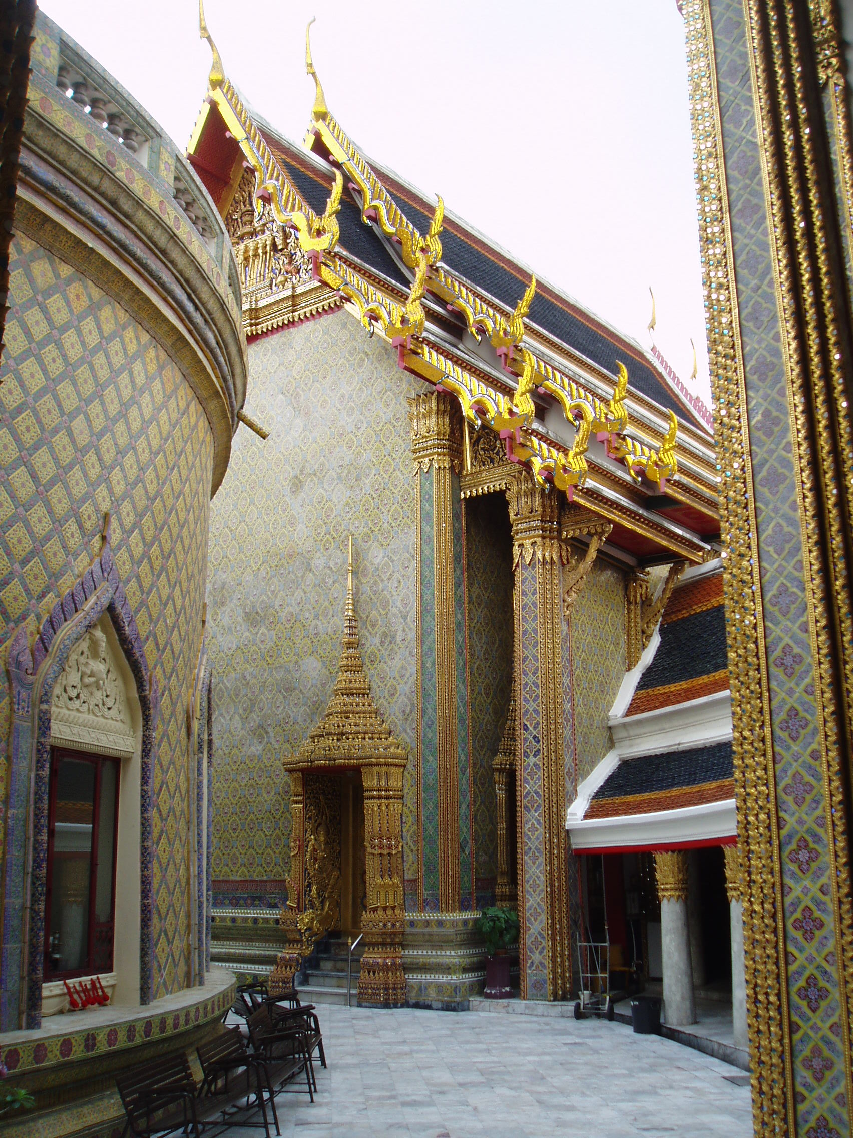 Wat Ratchabophit, Bangkok Wat Ratchabophit is one of the most unusual temples in Bangkok; built in the latter half of the 19th century it shows marked European influence in certain areas, such as the neo-gothic interior of the main bot (prayer hall) and many of the monuments in the adjoining Royal Cemetery, that includes a domed classical style tower and pinnacled gothic steeples amongst more traditional Thai and Khmer style structures. The centrepiece of the Temple is the huge tile-covered stupa that grows from the heart of the complex and is surrounded by a tight circular courtyard. The surrounding structures are richly decorated and gilded with typical Thai richness. The entrance gates to the temple compound have carved and painted door panels with bizarre figures that appear to be 'farang' (foreign/European) guards holding rifles! en.wikipedia.org/wiki/Wat_Ratchabophit