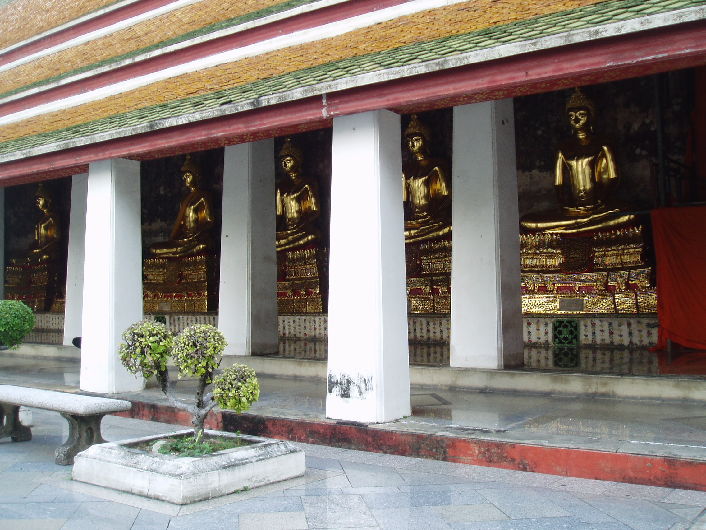 Buddha Gallery, Wat Suthat, Bangkok Wat Suthat is one of Bangkok's oldest and largest temples, having been built between the 1780s and 1820s. The complex consists of an impressive wihan (prayer hall) within a courtyard surrounded by a cloister containing many seated Buddha sculptures (as at Wat Pho). The wihan contains a large gilded Buddha and fine frescoes, but in common with the other temples we visited this day we didn't get any more than a glimpse of the interior as prayer sessions for the festival of Loi Kratong were in flow. The complex also has many interesting sculptures dotted about, including some elegant bronze horses, chinese figures and the most ridiculous looking farang ('foreigner' ,ie European) statues we saw (caricatures of 19th century British or French soldiers). In front of the Temple complex is a tapering wooden archway, all that remains of the 'great swing' from which terrifyingly dangerous rituals were performed in mid air at certain religious festivals in the 19th and early 20th centuries. www.sacred-destinations.com/thailand/bangkok-wat-suthat-a... bangkokforvisitors.com/suthat.html