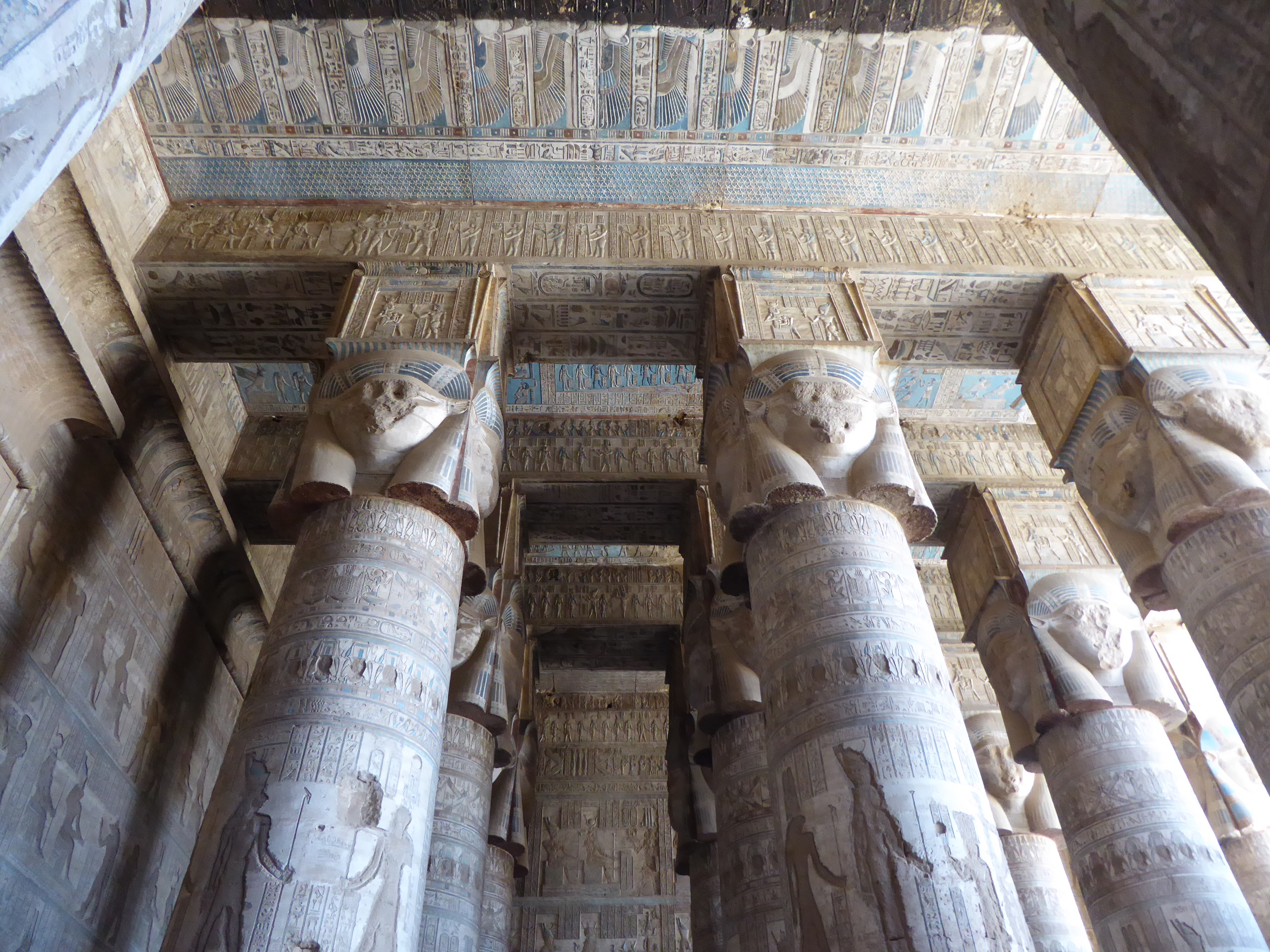 Temple of Hathor, Dendera The Temple of Hathor at Dendera is one of Egypt's best preserved and most beautiful ancient shrines. This magnificent edifice dates to the Ptolemaic period, late in Egyptian history, though the site long had been the cult centre for the goddess Hathor for centuries before (the earliest extant remains date to c360BC but a temple is recorded here as far back as c2250BC). Most of the main building dates to the reigns of the last Cleopatras and further decoration and building work within the complex continued in the Roman period up to the reign of Trajan. The dominant structure in the complex is the Temple of Hathor, an enormous structure with a rectangular facade punctuated by the Hathor-headed columns of the hypostyle hall within. This hall is an architectural wonder, a masterpiece of ancient Egyptian design and decoration, which covers every surface and has been recently cleaned, revealing a superb astrological ceiling in all its original vibrant colours. Sadly there was much iconoclasm here during the early Christian period and most of the reliefs of the walls and pillars have been defaced. Worse still is the damage to the 24 Hathor-head capitals: not one of the nearly a hundred huge faces of the goddess that once smiled down on this hall has been left unblemished, most with their features cruelly chiselled away. The main temple building is otherwise structurally intact, and extends into further halls and chapels beyond, again with much relief decoration (much of which is again defaced). In one corner is an entrance to a crypt below, an unusual feature in Egyptian temple architecture consisting of several narrow passages adorned with carved relief decoration in good condition. There are further sanctuaries and chapels above on the roof of the temple, accessed by a decorated staircase and including the room where the famous Dendera Zodiac was formerly located (today its place in the ceiling taken by a cast of the original, now displayed in Paris). The highest part of the roof complex is no longer accessible to tourists, but I can still recall making the ascent there on our first visit in 1992. Several other buildings surround the main temple, the most impressive of which is the mammisi or 'birth-house'. This consists of a large rectangluar hall surrounded by a colonnade near the entrance to the site and has some well preserved relief decoration on its exterior. Most of this structure dates to the Roman period, but the ruins of its predecessor built under Nectanebo II (Egypt's last native pharoah) stand nearby. Dendera temple is one of the most rewarding in Egypt and shouldn't be missed. It is one of the most complete and evocative ancient monuments in the country and its recent restoration has revealed a surprisingly extensive amount of colour surviving within (we were amazed by the dramatic contrast with the soot-blackened ceiling we'd beheld on our previous visit in the 1990s). Despite its relative youth (in Egyptian terms at least!) it is easily one of my favourite sites in Egypt. en.wikipedia.org/wiki/Dendera_Temple_complex