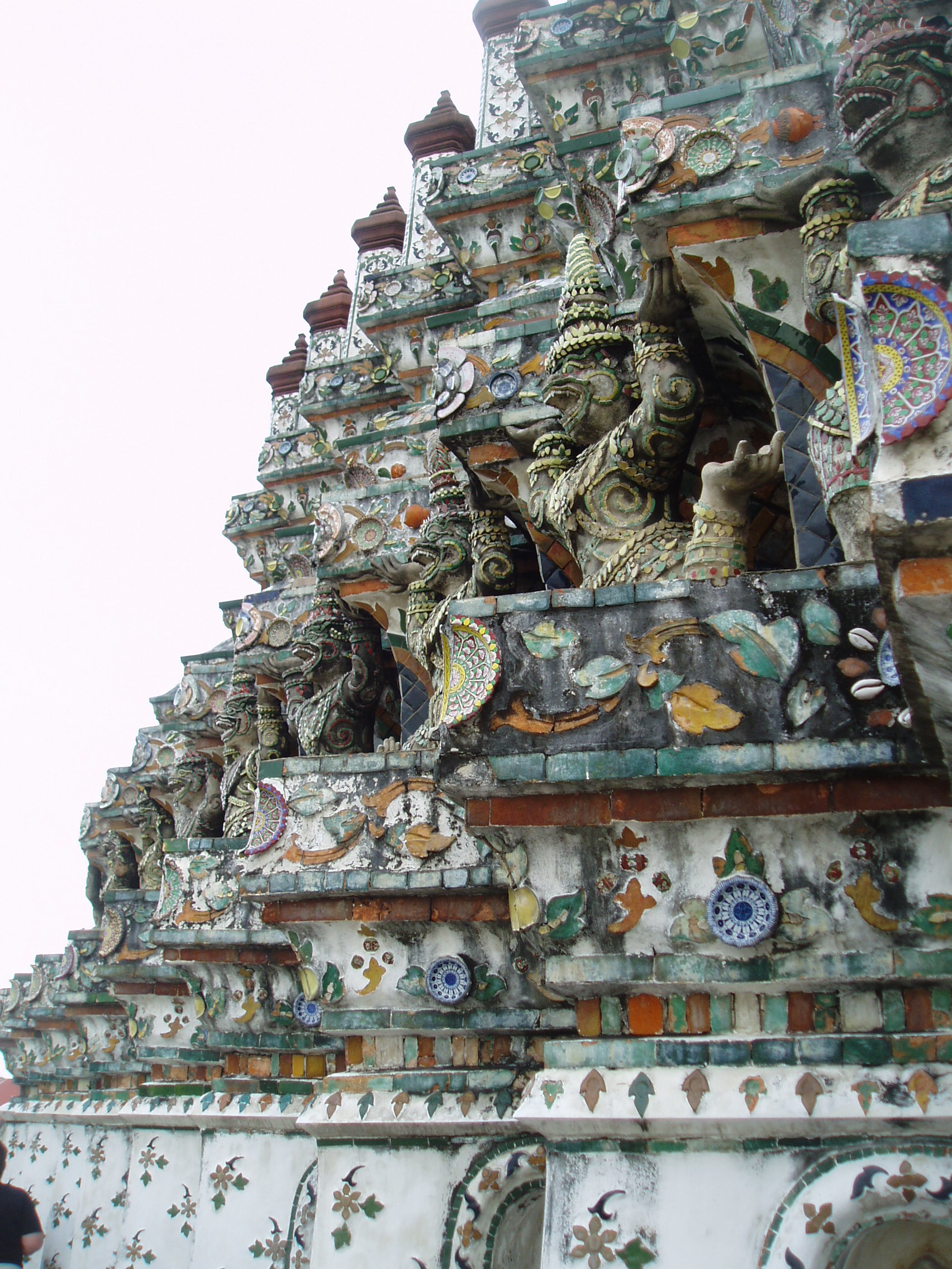 Wat Arun, Bangkok Located close to the Chao Phraya riverfront on Bangkok's west bank, Wat Arun (the Temple of Dawn) is one of the city's most prominent landmarks; it's towering steeple-like stupa, surrounded by four smaller spires known as prangs, forms a unique shilouette, at first as reminiscent of a gothic cathedral as a normal Thai temple. The temple itself is located behind the stupa/pagoda and is a fairly extensive complex founded in the late 18th century, but it is generally the giant spire-stupa, built in the first half of the 19th century, that visitors focus on. The monument is almost entirely encrusted with porcelain mosaic decoration which extends to much of the figure sculpture (rows of crouching demons, monkey warriors and apsaras can be seen propping up the tower at various levels). Two terraces, one and two thirds up respectively, afford spectacular views over the temple complex and across the Chao Phraya and city centre beyond. The upper level however is only accessible via a terrifyingly steep staircase! en.wikipedia.org/wiki/Wat_Arun