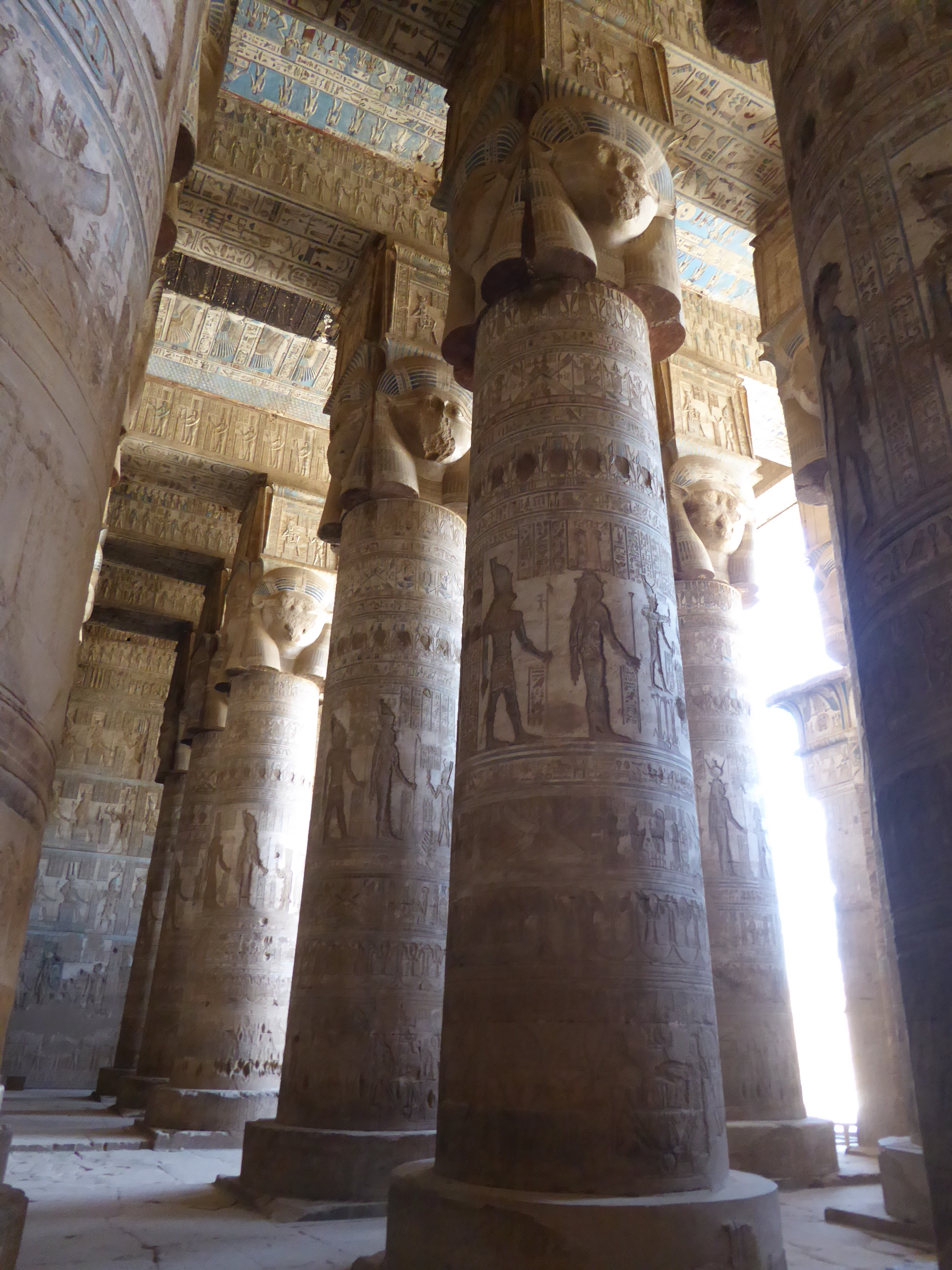 Hypostyle Hall, Dendera Temple The Temple of Hathor at Dendera is one of Egypt's best preserved and most beautiful ancient shrines. This magnificent edifice dates to the Ptolemaic period, late in Egyptian history, though the site long had been the cult centre for the goddess Hathor for centuries before (the earliest extant remains date to c360BC but a temple is recorded here as far back as c2250BC). Most of the main building dates to the reigns of the last Cleopatras and further decoration and building work within the complex continued in the Roman period up to the reign of Trajan. The dominant structure in the complex is the Temple of Hathor, an enormous structure with a rectangular facade punctuated by the Hathor-headed columns of the hypostyle hall within. This hall is an architectural wonder, a masterpiece of ancient Egyptian design and decoration, which covers every surface and has been recently cleaned, revealing a superb astrological ceiling in all its original vibrant colours. Sadly there was much iconoclasm here during the early Christian period and most of the reliefs of the walls and pillars have been defaced. Worse still is the damage to the 24 Hathor-head capitals: not one of the nearly a hundred huge faces of the goddess that once smiled down on this hall has been left unblemished, most with their features cruelly chiselled away. The main temple building is otherwise structurally intact, and extends into further halls and chapels beyond, again with much relief decoration (much of which is again defaced). In one corner is an entrance to a crypt below, an unusual feature in Egyptian temple architecture consisting of several narrow passages adorned with carved relief decoration in good condition. There are further sanctuaries and chapels above on the roof of the temple, accessed by a decorated staircase and including the room where the famous Dendera Zodiac was formerly located (today its place in the ceiling taken by a cast of the original, now displayed in Paris). The highest part of the roof complex is no longer accessible to tourists, but I can still recall making the ascent there on our first visit in 1992. Several other buildings surround the main temple, the most impressive of which is the mammisi or 'birth-house'. This consists of a large rectangluar hall surrounded by a colonnade near the entrance to the site and has some well preserved relief decoration on its exterior. Most of this structure dates to the Roman period, but the ruins of its predecessor built under Nectanebo II (Egypt's last native pharoah) stand nearby. Dendera temple is one of the most rewarding in Egypt and shouldn't be missed. It is one of the most complete and evocative ancient monuments in the country and its recent restoration has revealed a surprisingly extensive amount of colour surviving within (we were amazed by the dramatic contrast with the soot-blackened ceiling we'd beheld on our previous visit in the 1990s). Despite its relative youth (in Egyptian terms at least!) it is easily one of my favourite sites in Egypt. en.wikipedia.org/wiki/Dendera_Temple_complex